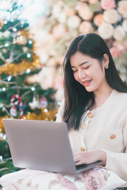 Portrait freiberuflich tätiges schönes positives Lächeln junge asiatische Frau, die online mit Laptop-Computer zu Hause im Wohnzimmer im Innenbereich arbeitet Dekoration Während der Weihnachts- und Neujahrsferien.