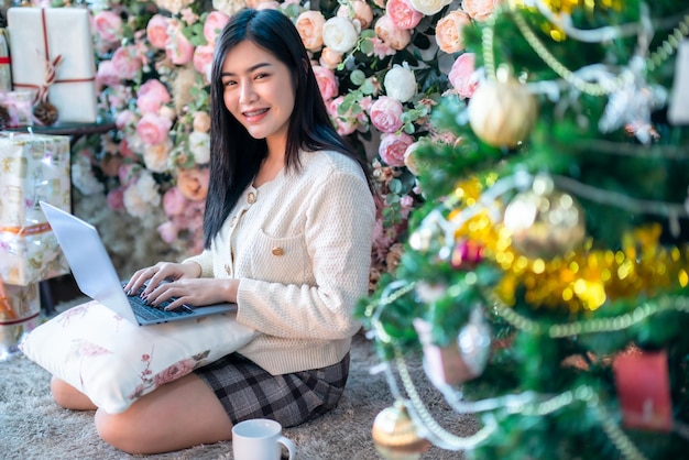 Portrait freiberuflich tätiges Unternehmen schönes positives Lächeln junge asiatische Frau online arbeiten mit Laptop-Computer zu Hause im Wohnzimmer drinnen Dekoration während der Weihnachts-, Weihnachts- und Neujahrsferien