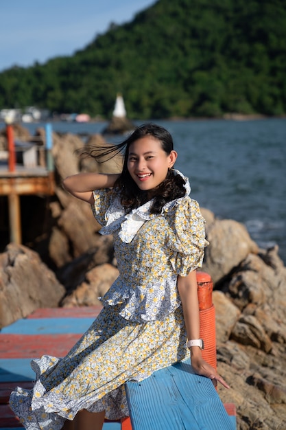 Portrait glückliche asiatische Frau Touristen sitzen auf der Brücke mit Meerblick an der Pagode im Meer am windigen Tag