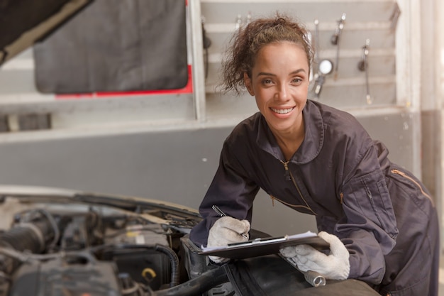 Portrait glücklicher Arbeiter Afroamerikanerfrauenarbeit für Automechaniker in der Garage, die Automotor überprüft.