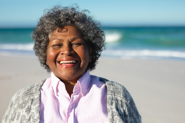 Portrait in Nahaufnahme einer älteren afroamerikanischen Frau, die am Strand mit blauem Himmel und Meer im Hintergrund steht und zur Kamera lächelt