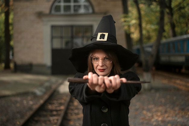 Portrait junge Frau im Hexenkostüm hält Zauberstab vor ihrer Halloween-Party School of Magic