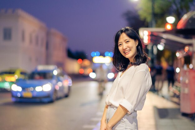 Foto portrait junge schöne asiatische frau, die während der fahrt durch die bangkok street twilight lächelt