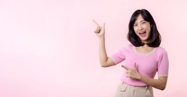 Foto portrait junge schöne asiatische frau glückliches lächeln, das mit dem finger und der hand zeigt, um auf dem kopierbereich zu zeigen, der auf rosa hintergrund isoliert ist attraktive weibliche person geste aufmerksamkeit auf diese förderung