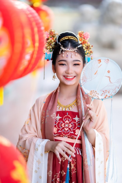 Portrait Lächeln Süßes kleines asiatisches Mädchen in chinesischen Kostümen und mit chinesischer Fandekoration für das chinesische Neujahrsfest feiern die Kultur Chinas am chinesischen Schrein Öffentliche Orte in Thailand