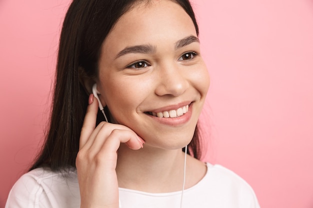 Portrait Nahaufnahme eines optimistischen hübschen Mädchens mit Kopfhörern, das lächelt, während es Musik hört, isoliert über rosa Wand