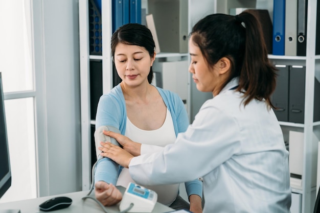 Portrait Ärztin legt die Manschette um den Arm der werdenden Patientin, um ihren Blutdruck während der Schwangerschaftsuntersuchung im Krankenhaus zu überwachen.