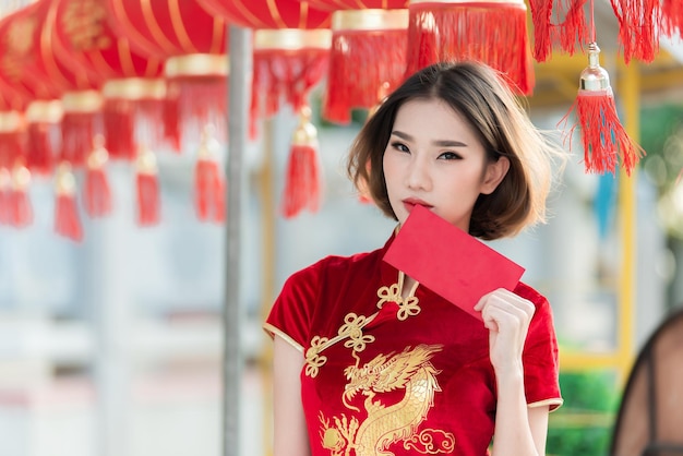 Portrait schöne asiatische Frau in Cheongsam-KleidThailänderFröhliches chinesisches NeujahrskonzeptFröhliche asiatische Dame in traditioneller chinesischer Kleidung mit einem roten Umschlag