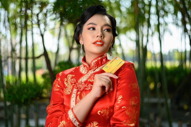 Portrait schöne asiatische Frau in einer chinesischen Cheongsam-Pose mit Kreditkarte auf Bambuswald