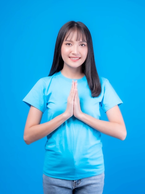 Portrait schöne asiatische junge Frau, thailändisches Mädchen knallt Frisur Respekt, Sawasdee Symbol aus Thailand Grußkultur für Hallo oder Auf Wiedersehen einzeln auf blauem Hintergrund