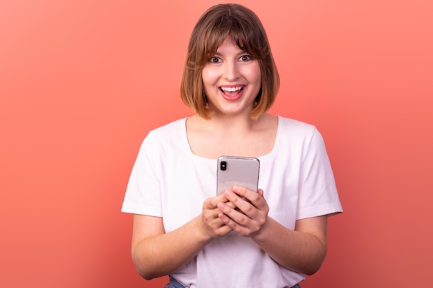 Portrait schöne, erstaunte, fröhliche, braunhaarige Frau, die ein Telefongerät als Reaktion der Freude benutzt