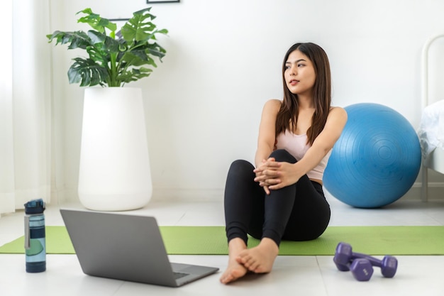 Portrait Sport asiatische Schönheit Körper schlanke Frau in Sportkleidung sitzend entspannen und Mädchen Yoga praktizieren und Fitness-Übungen mit Laptop-Computer im Schlafzimmer zu Hause machenDiät-KonzeptFitness und gesund