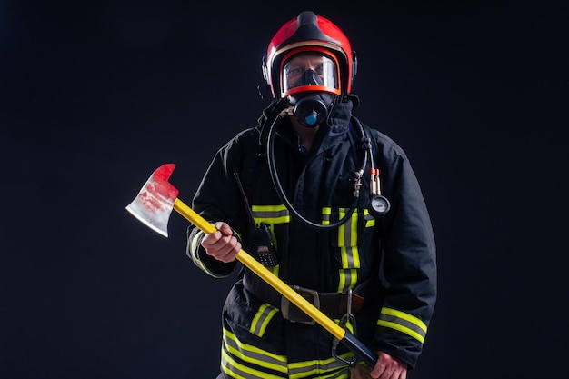 Portrait starker Feuerwehrmann in feuerfester Uniform, der eine Axt in seinen Händen hält, schwarzes Hintergrundstudio