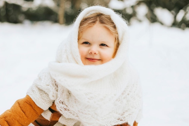 Portrait süßes kleines Mädchen Kleinkind im weißen russischen Stil Orenburg Schal Schal im Schnee Winterwald Konzept der Weihnachtsferien und des neuen Jahres im Retro-Vintage-Stil