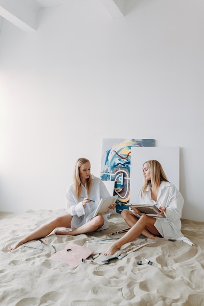 Portrait von glücklichen Zwillingsmädchen Künstlerinnen Schwestermädchen in einem Fotostudio auf dem Sand