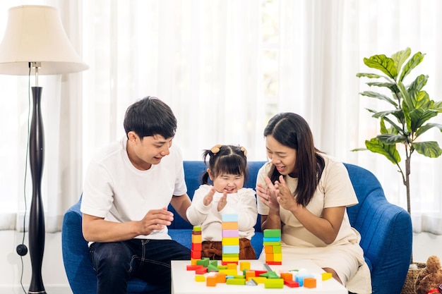 Portrait von glücklicher Liebe asiatischer Familienvater und Mutter mit lächelnder Aktivität des kleinen asiatischen Mädchens Lernen und Geschicklichkeits-Gehirntraining spielen mit Spielzeugbau-Holzklötzen-Brettbildungsspiel zu Hause