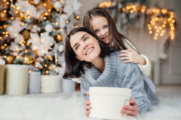 Portrait von glücklicher Mutter und Tochter verbringen Freizeit zusammen, umarmen sich, haben ein angenehmes Lächeln, halten verpackte Geschenkboxen, feiern Neujahr oder Weihnachten zusammen