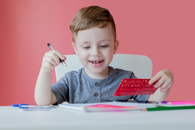 Portrait von niedlichen Jungen zu Hause machen Hausaufgaben Kleine konzentrierte Kinder schreiben mit bunten Bleistift drinnen Grundschule und Bildung Kid lernen Schreiben von Buchstaben und Zahlen