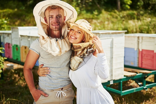 Portrait von zwei schönen Imkern. Steht zusammen in der Nähe der Bienenstöcke. Süßes Paar umarmt sich.