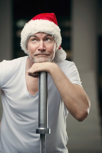 Foto portraite des älteren mannes im weihnachtsmann-hut in der turnhalle silvester und weihnachtskonzept