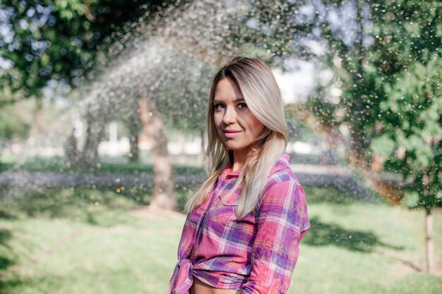 Portraitfoto einer erwachsenen, glänzenden blonden Frau, die im Park steht und ein kariertes Hemd trägt, das im Bauch gebunden ist ...