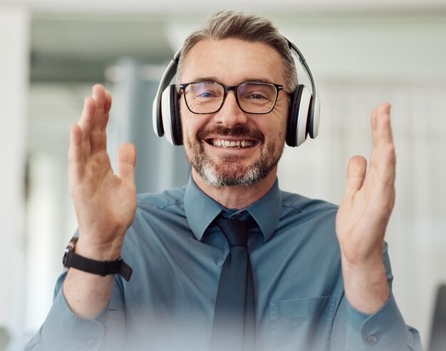 Portraitgeschäft und Mann applaudieren beim Videoanruf, lächeln und Kopfhörer zu Hause. Fröhliches Klatschen ins Gesicht und Webinar eines reifen Managers mit Brille bei virtuellen Meetings, Online-Feiern oder Fernarbeit