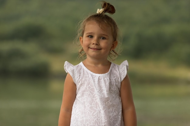 Portrat eines süßen kleinen Mädchens in einem weißen Kleid steht an einem Sommerabend im Gras am Ufer eines Sees Sonnenuntergang am See