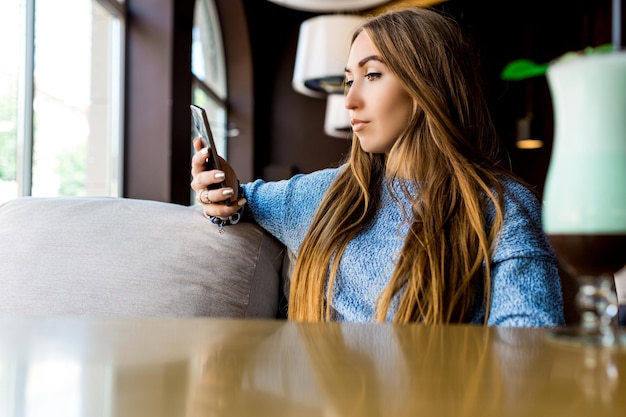 Portret der jungen Frau, die SMS am Telefon im Café liest, tonte selektiven Fokus