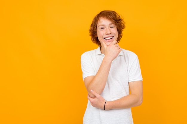 Portret eines rothaarigen gutaussehenden lächelnden nachdenklichen kaukasischen Teenager-Mannes in einem weißen T-Shirt auf einem gelben Hintergrund