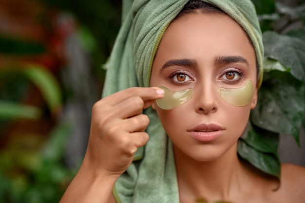 Portret foto de una lujosa mujer de ojos marrones que se quita parches de los ojos.