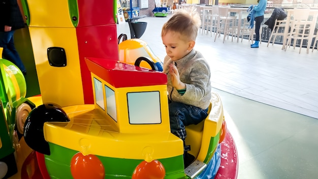 Portriat de alegre niño pequeño cabalgando sobre un colorido carrusel con barcos de juguete en el parque de atracciones en el centro comercial