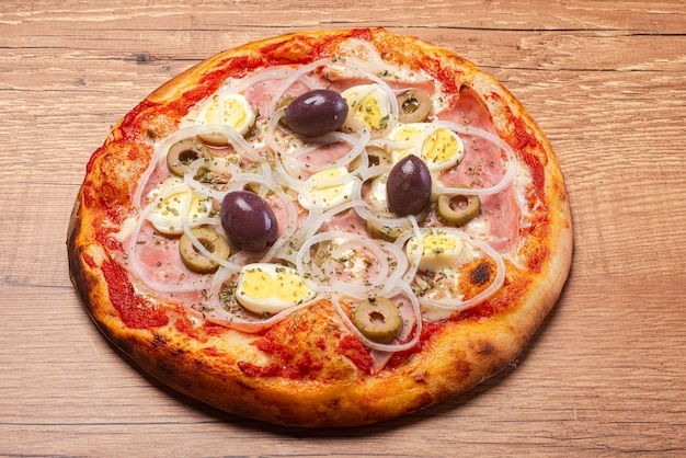 Portugiesische Pizza mit Schinken, Käse, Eiern, Zwiebeln und schwarzen Oliven, serviert auf einem rustikalen Holztisch.