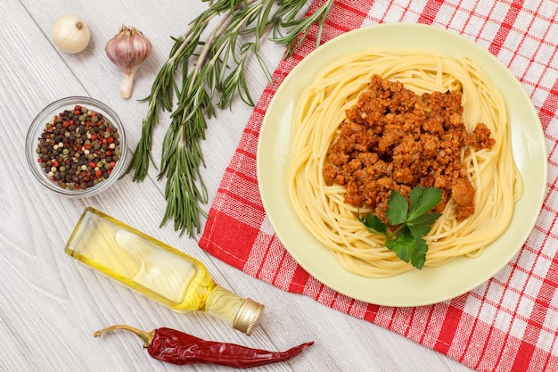 Porzellanteller mit Spaghetti Bolognese auf Küchenserviette. Gewürze und Kräuter auf Holzbrettern. Ansicht von oben.