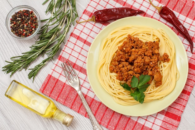 Porzellanteller mit Spaghetti Bolognese auf Küchenserviette. Gewürze und Kräuter auf Holzbrettern. Ansicht von oben.