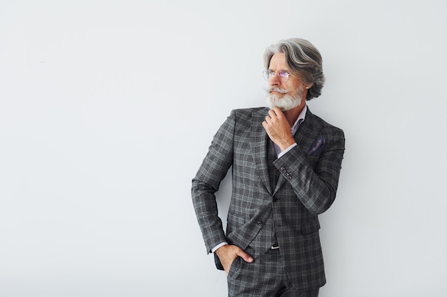 Posando para la cámara Senior hombre moderno con estilo con pelo gris y barba en el interior