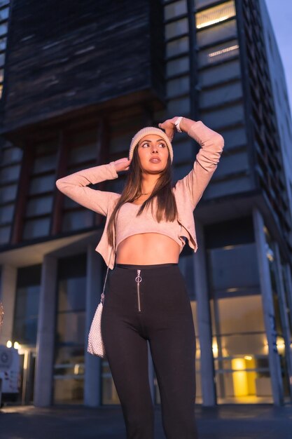 Posando en la ciudad en una noche de invierno con un suéter y un sombrero de punto rosa