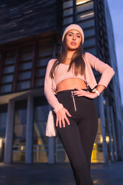 Posando en la ciudad en una noche de invierno con un suéter y un sombrero de punto rosa