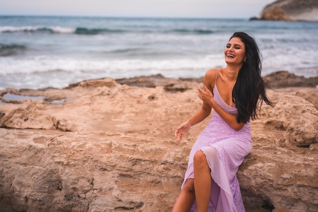 Posando de una joven morena caucásica con un vestido rosa en la playa divirtiéndose junto al mar