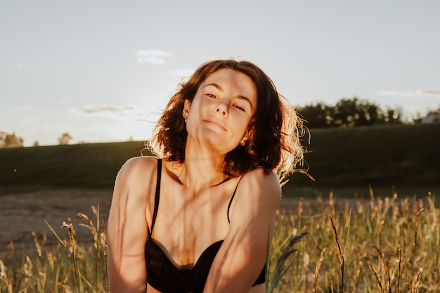 Posando mujer en la naturaleza. La puesta del sol iluminada por el sol de la mujer joven sonríe y pensó contra el contexto del bosque d y el campo.