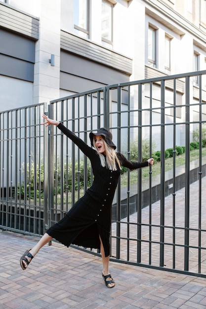 Posando mulher loira coberta de preto pendurado em uma cerca de trilho em uma pose de dança