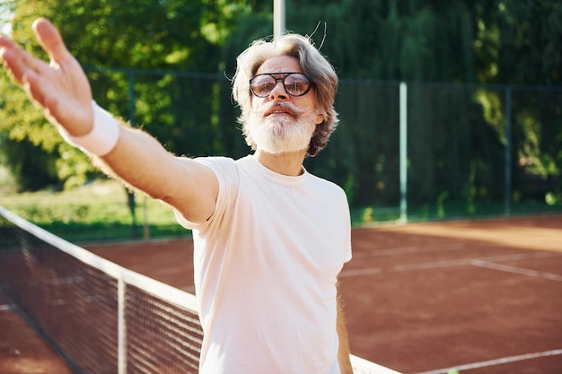 Foto posando para uma câmera em óculos de sol homem elegante moderno sênior ao ar livre no campo esportivo durante o dia