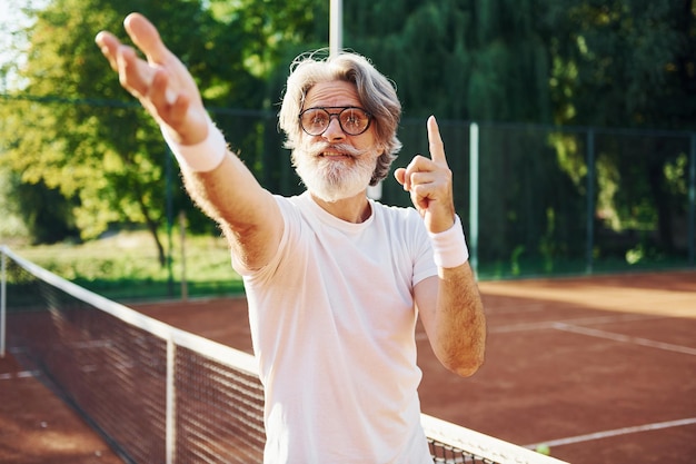 Foto posando para uma câmera em óculos de sol homem elegante moderno sênior ao ar livre no campo esportivo durante o dia