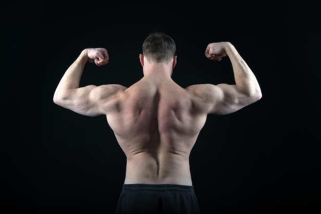 Pose de culturista atlético en pantalones aislados sobre fondo negro Entrenador deportista con el pecho desnudo Hombre con cuerpo musculoso espalda y bíceps Deporte y entrenamiento Dieta y salud física