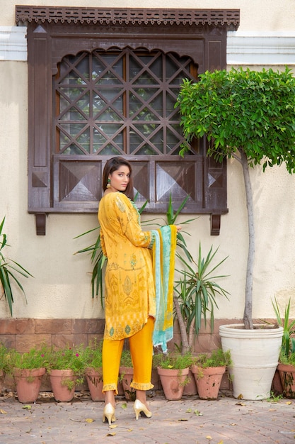 Pose de espalda de chica de cabello rubio caliente para sesión de fotos al aire libre con plantas con vestido amarillo tradicional