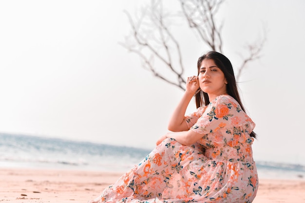 Pose frontal de menina bonita alegre casual sentada na praia modelo paquistanês indiano