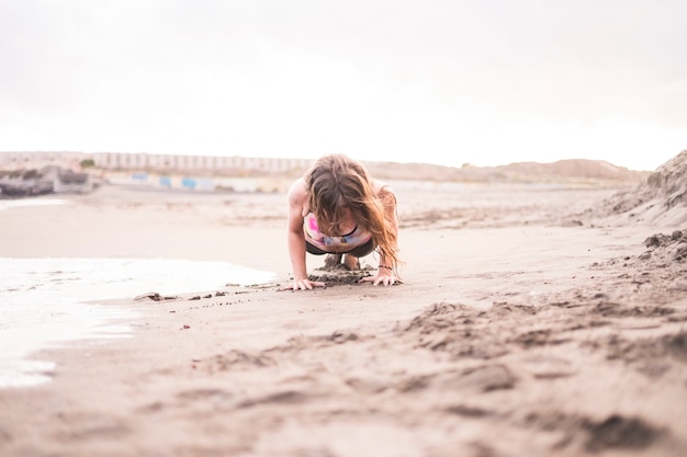 Posição de prancha dura na costa perto das ondas do oceano. boa atividade esportiva ao ar livre em contato com a natureza e a areia. corpo saudável para uma bela jovem bonita ficar bem com fitness. posição centrada