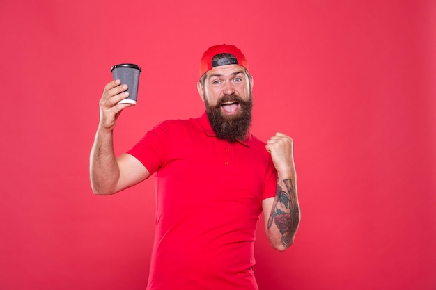 Posição de trabalho do barista Funcionários da cafeteria queriam bebida preparada para você Barista alegre Barista homem barbudo boné vermelho uniforme segurar xícara de café de papel Barista recomenda bebida com cafeína