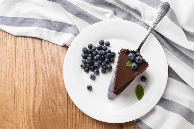 Posição plana da fatia de bolo de chocolate no prato com mirtilos