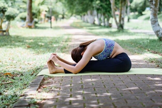 Posición practicante de la yoga de la mujer asiática en el parque