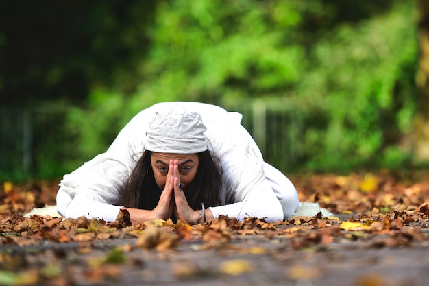 Posición de yoga entre las hojas de otoño en el parque.